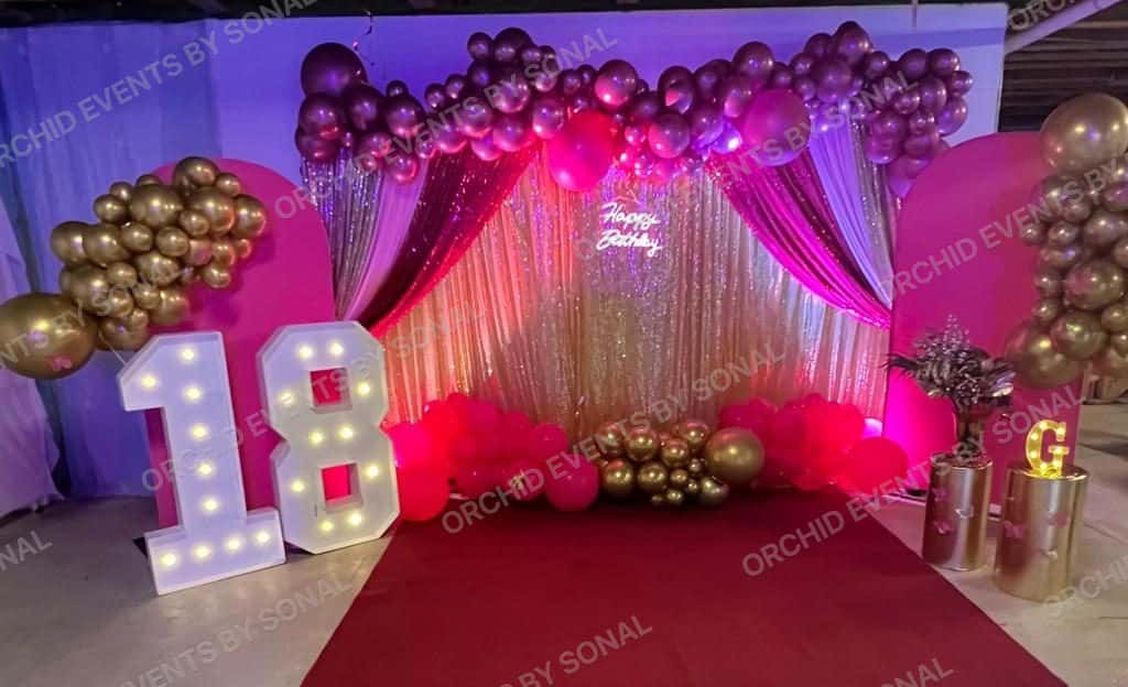 Magenta and gold birthday stage with a lit 18 marquee, balloon garland and draped backdrop