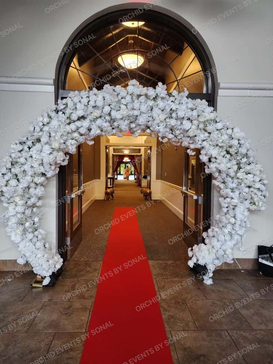 White blossom arch over a red carpet at the entrance to a temple hall