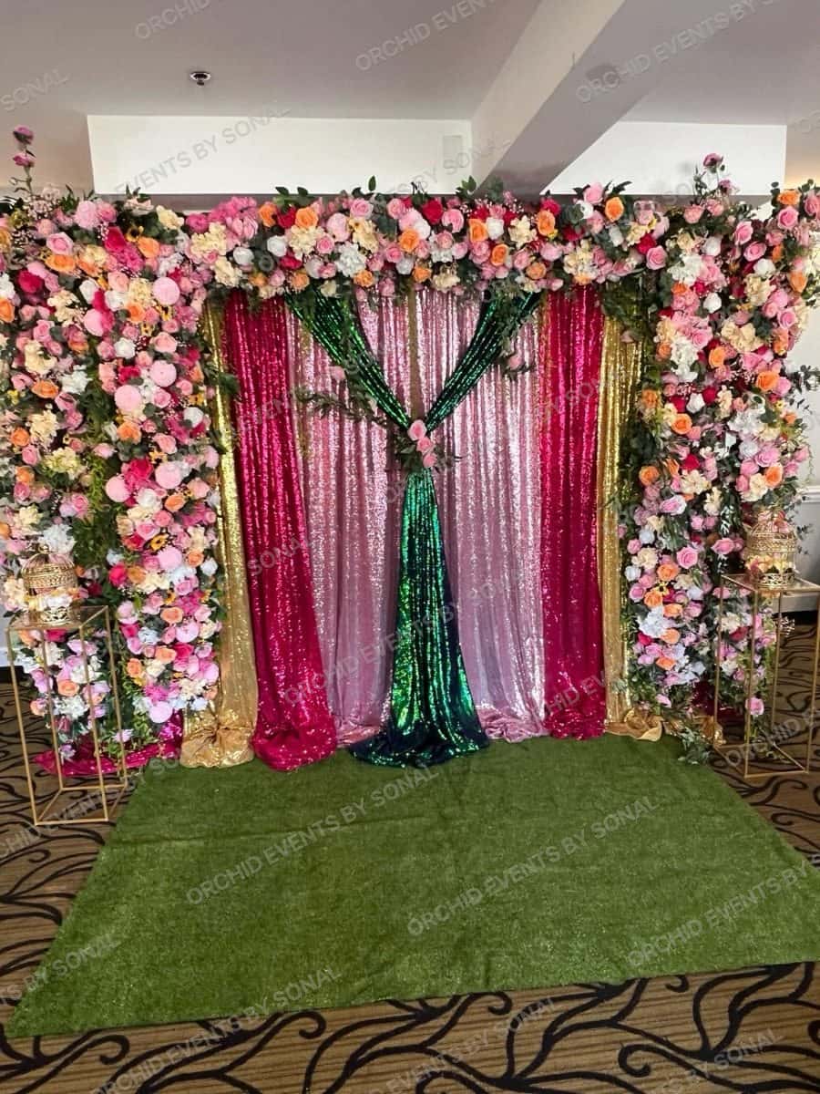 Stage framed by a pastel flower wall with magenta and green sequin drapes at the centre