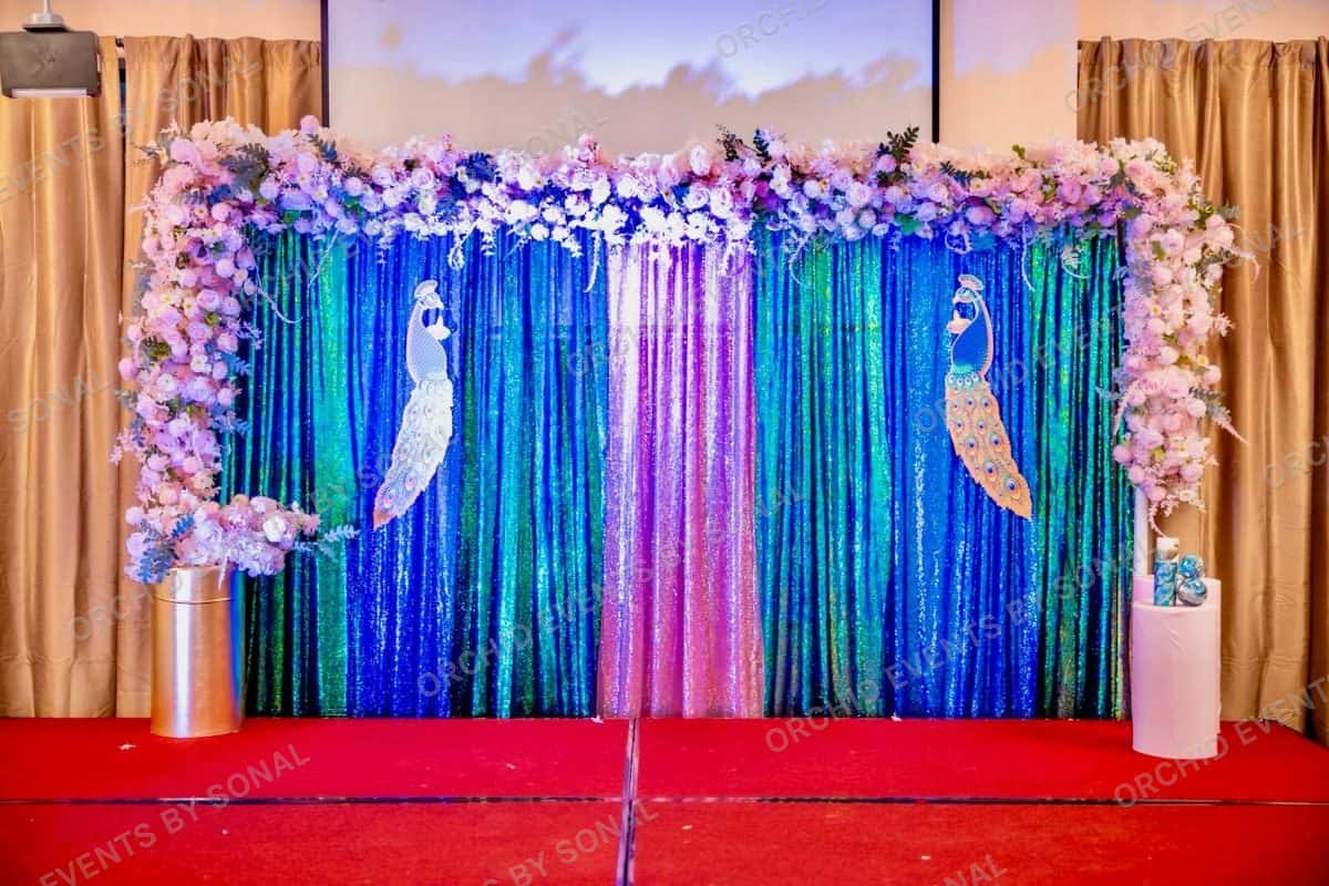 Sangeet backdrop in blue and teal sequin with two standing peacocks and a blossom arch